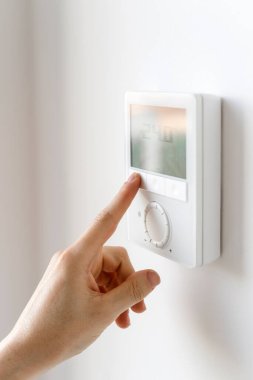 Merkezi ısıtma ya da klimanın klimasını ayarlamak için dijital paneli olan ev termostatı. Kadın elinin dikey çekimi dairede konfor sıcaklığını seç, manzarayı kapat