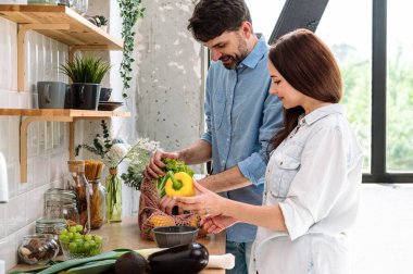 Marketten alışveriş yapıyorum. Gülümseyen koca, eşiyle birlikte alışveriş çantalarını açıyor, biber tutuyor, mutfaktaki masaya sebze koymaya yardım ediyor. Yemek pişirme ve yeme konsepti için taze ürünler