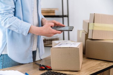 Kutusunda akıllı telefon tarama etiketi olan kadın girişimci görüntüsü. Depoda çalışan serbest çalışan bir kadın ve gönderilmek üzere paketler hazırlıyor. Ticari konsept