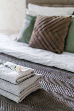 Gül çiçeğiyle süslenmiş ve otel odasındaki konforlu yatağın üzerine katlanmış temiz terry havlularına yakın çekim. Şatafatlı yatak odası ve temiz çarşaflar. Konaklama kavramı.