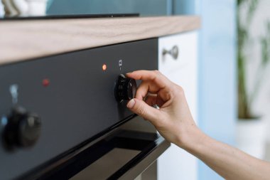 Kadın ev hanımlarının el kameraları kontrol panelinin düğmesini kullanarak elektrikli fırını açar ve evde yemek pişirmek için program ya da sıcaklık modunu seçer. Modern ev aletleri mutfakta..