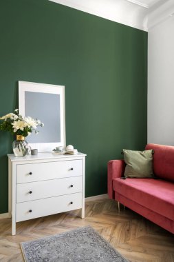 Dairenin iç dekorasyonunda klasik stilin dikey çekimi. Kırmızı kanepenin yanında yeşil duvarlı yastıklı resim çerçeveli beyaz tuvalet. Evdeki ahşap zeminde mobilyalar..