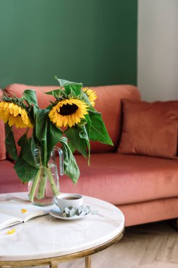 İçinde çay olan mermer masaya seçici bir odak, bulanık oturma odasına karşı sarı ayçiçekli defter ve cam vazo. Konforlu evde kahvaltı. Sabah konsepti.