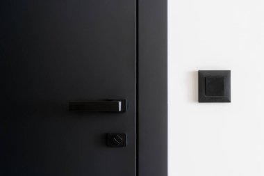 Metal saplı, kapalı gri kapının yanındaki beyaz duvardaki siyah ışık düğmesine yakın çekim. Detaylar modern dairenin iç unsurları. Oda girişi. Kilitli ofis