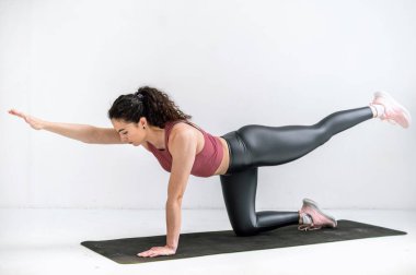 Spor tişörtlü ve taytlı genç bir kadın yoga yapıyor. Stüdyoda spor minderinde kuş pozu veriyor. Vücut dengesi, koordinasyon egzersizleri. Evde beden eğitimi.
