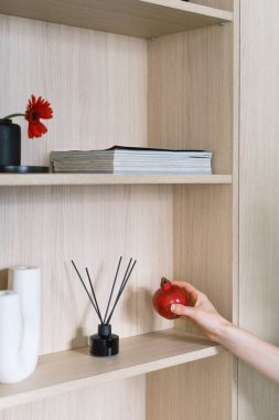 Bej rengi ahşap bir dolabın yanında elinde şık dekoratif malzemeyle dikey bir kadın resmi. Ev içi detaylar. Modern dairede yaşam alanı ayarlamak.