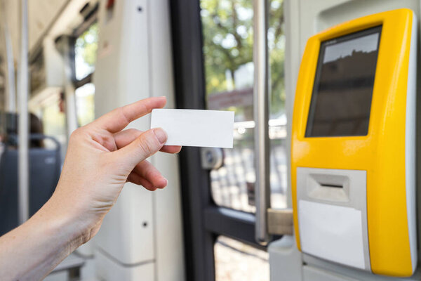 Selective focus on woman hand with blank paper ticket inside public transport or intercity train. Passenger preparing to validate travel document in modern validator.