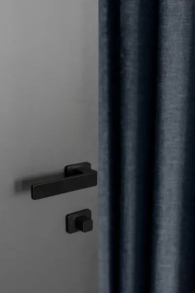 Vertical shot of black metal handle and open door in apartment. Entrance in living room. Privacy and security concept. Element of interior in modern house.