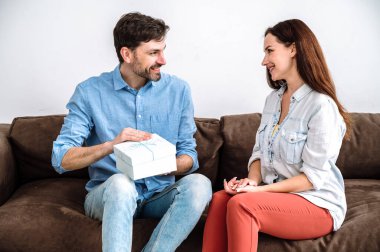 Gülümseyen adamın hediyeli bir kutu almasına ve kanepede karısıyla otururken açmasına sevindim. Genç kadın kocasını doğum günüyle kutladı, ona sevgi ve ilgi gösterdi..