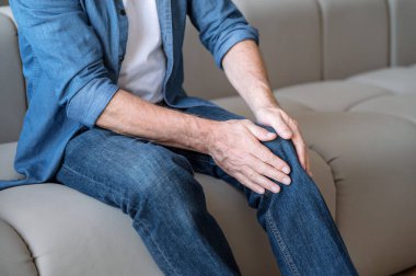 Son sınıf öğrencisi dizinde ani bir ağrı hissediyor. Gergin sakatlık. Evdeki kanepede oturan erkek, eklem iltihabı, kemik hastalığı osteoporoz veya iltihaplanma sürecinden muzdarip..