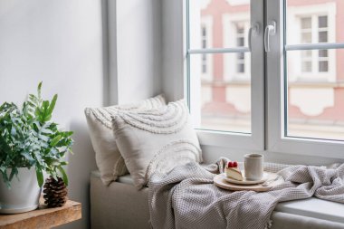 Pencere kenarında ev dekorasyonu ve lezzetli kahvaltılı ahşap pano olan rahat bir yer. Dairenin iç tasarımında Hygge stili. Penceresinde battaniye olan rahat bir ev odası. Sabah kahvesinin tadını çıkarıyorum..