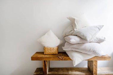Tahta bankta beyaz yastık kılıflarının içinde yastığa yakın küçük yastıklı hasır çamaşır sepeti. Yıkama ve temizlik kavramları. Yatak odasının içi şık ev dekorasyonu elementleriyle dolu.