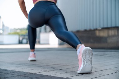 Spor giyimli, genç, yetişkin bir kadının spor ayakkabılarına odaklan. Şehir dışında sporcu kadın antrenmanı. Sporcu kadın antrenmandan önce vücudunu esnetiyor.