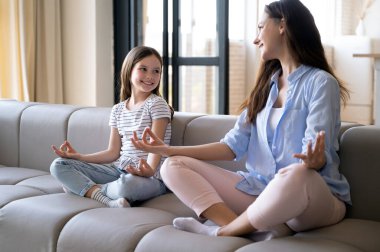 Mutlu gülümseyen çocuk rahat koltukta oturup annesine bakıyor, evde yoga yapıyor. Meditasyon yapmak, ev içi sağlık faaliyetlerinin keyfini çıkarmak..