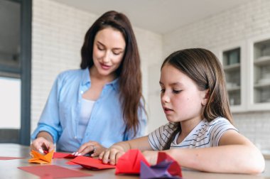 Masa başında otururken ve evde boş vakitlerinde origami yaparken çoklu renkli kağıtları katlamaya odaklan. Anne çocuğa yardım ediyor. El işi faaliyetleri
