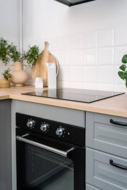 Dolaba entegre edilmiş elektrikli fırının yan görüntüsü ahşap tezgah, indüksiyon cam seramik soba ve modern iç mimariye sahip iç mutfağa döşenmiş beyaz fayanslı duvar. Ev aletleri konsepti