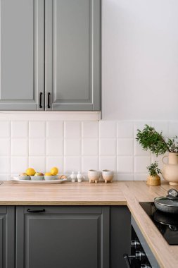 Klasik stil mutfağında gri iç döşemeli dikey görüntü. Ahşap dolap ve tezgah, yeşil dallı seramik vazo sürahi, mutfak gereçleri, konforlu dairede taze meyve tabağı..