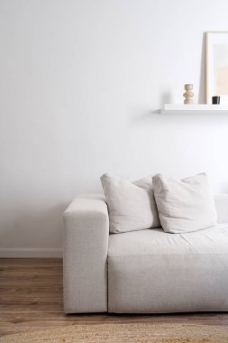 Minimalist evde modüler mobilyalar. Oturma odasında beyaz telif duvarına yaslanmış yastıklı rahat kanepenin dikey çekimi. Modern apartmanda iç dizayn. Koltuğun üzerinde dekorasyon var.
