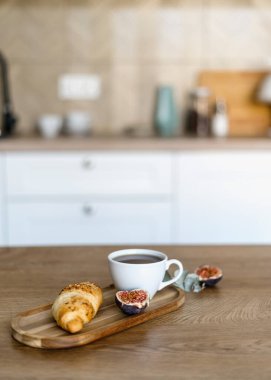 Modern evdeki ahşap mutfak adasında nefis bir kahvaltıya odaklan. Kahve bardağı, bambu tepside taze fırın bulanık iç tasarıma karşı. Sabah konsepti.