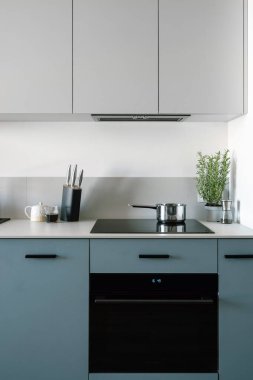 Elektrikli fırının ön manzarası, tencereli cam seramik fırın üstü, modern dolap, mutfak tezgahında mutfak gereçleri ve minimalist iç mekan. Yemek pişirmek için ev aletleri