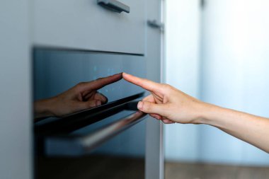 Yemek pişirmek için modern elektrikli fırının el sensör düğmesine basılı kadın görüşü. Kadın parmak göstergeleri ile dokunmatik kontrol panelinde program seçin. Mutfakta ev yapımı fırın aletleri.