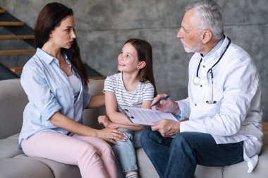 İlaç ve sigorta konsepti. Tecrübeli aile doktoru annesiyle birlikte küçük bir hastayı ziyaret eder, konuşur, soru sorar, sağlık kontrolüyle form doldurur. Erkek çocuk doktoru, evdeki muayenede çocuğu muayene ediyor.