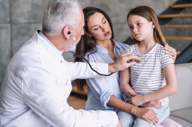 Hasta kızı muayene eden doktor doktor, ev ziyareti sırasında steteskop kullanarak nefes alan çocuk doktoru. Üzgün çocuk kendini iyi hissetmiyor ve bronşit belirtileri gösteriyor. Önleme zatürree kavramı.