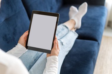 Kadın elinin kırpılmış görüntüsü taşınabilir dijital cihazla birlikte ekrana yansıtılır. Evdeki rahat koltukta uzanmış, rahat giysiler giymiş, tablette kitap okuyan bir kadının omuzlarının üstünden. Kopyalama alanı olan Gadget