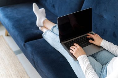 Boş ekranlı ya da boş ekranlı modern dizüstü bilgisayar kullanan bir kadın görüntüsü. Klavyede yazan kızın omuz manzarası, internet günlüğü, koltukta uzanan bilgisayardaki arama bilgileri