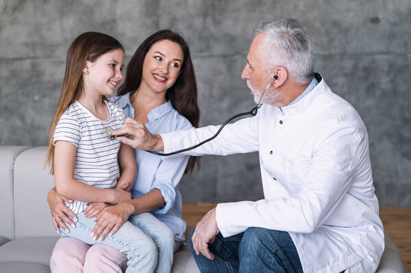 Заботливый семейный врач держит стетоскоп, прислушивается дыхание и сердцебиение в груди счастливой пациентки. Молодая мать с маленькой дочерью проверяет обследование у педиатра. Концепция здравоохранения