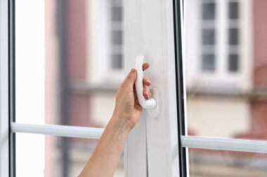 Seçici odak noktası, dairedeki beyaz plastik pencereyi açan bir kadın eli. Bulanık arka plan. Evdeki havalandırma odası. Havalandırma kavramı.