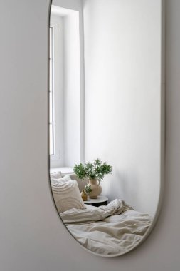 Yatak odasındaki detaylar modern ışık içerikli ve boho tarzı elementler, yatağın yansıması yumuşak çarşaf ve yastıklar, komodin masası seramik sürahi vazo ve yeşil bitki..