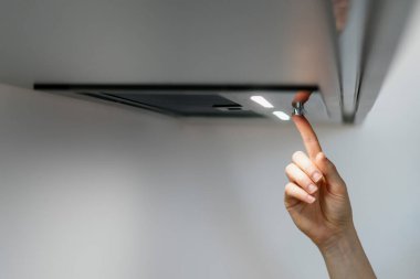 Kadın, kaputtaki el düğmesine basar, havalandırma için sessiz modu seçer. Modern sökücünün kontrol panelinde bir kadın aydınlatma ışığını açıyor. Evde profesyonel mutfak aletleri var.