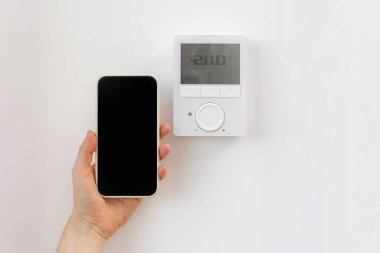 Kadının kapalı odanın sıcaklığını kontrol etmek için akıllı telefondaki uygulamayı kullanırken çekilmiş bir fotoğrafı. Cep telefonundaki cep telefonu uygulamasında ev ısıtma termostatı yönetmeliği. Akıllı ev kavramı