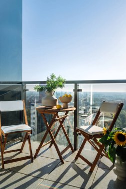 Şehir merkezinin manzarasıyla birlikte balkonun dikey görüntüsü. Boş masa, sandalyeler ve şeffaf bölmelere karşı diğer dekorasyonlar.