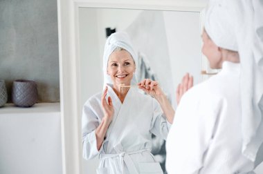 Çekici gülüşlü bir kadın aynaya bakıyor ve dişlerini bambu diş fırçasıyla fırçalıyor. Beyaz, düz, sağlıklı dişler. Ağız temizliği kavramı. Günlük sabah rutini.