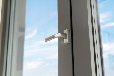 Daireye gri metal çerçeveli ve gümüş saplı modern pvc pencere. Kapı tokmağına odaklan. Şeffaf camdan mavi gökyüzü görüntüsü