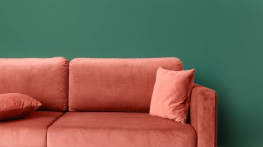 Mercan konforlu kanepeyi kapatın. Fotokopi alanı olan yeşil duvarlı yastıklar. Evdeki oturma odasında modern zarif mobilyalar. Temiz, yumuşak döşeme koltuğu, web pankartı manzarası