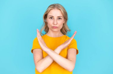 Mavi stüdyo arka planında fotokopi alanı olan çapraz elli dur işareti gösteren ciddi bir kadın. İstismarı, ayrımcılığı, şiddeti reddeden bir kadın. Anlaşmazlık