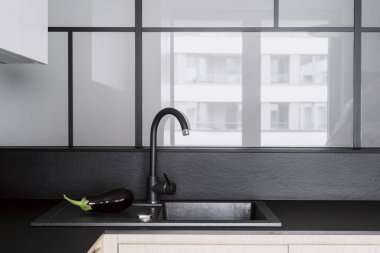 Siyah metal musluğu kapatın ve mermer tezgahta inşa edilmiş modern lavaboyu cam duvar zemininde fotokopi alanı ile kapatın. Evin içinde zarif bir mutfak var..