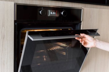 Elektrikli fırının kapağını açıp evde yemek pişiren kadın görüntüsü. Ev aletleri kavramı, mutfak malzemeleri. Yemek ısıtmak için mikrodalga kullanan bir kadın.