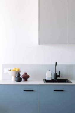 Modern çatı katının evdeki mutfağın dikey görüntüsü. Gri dolabın altında musluğu olan siyah seramik lavabo. Tezgahında meyve olan dekoratif vazolar. Boşluğu kopyala.