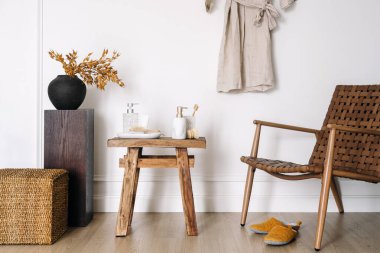 Dispanser şişeleri, diş fırçaları, diş macunu, mesaj fırçası ve nemlendirici kremle ayakta durun. Modern banyo dekorasyonu, ahşap mobilyalar, hasır sandalye, çamaşır sepeti, keten bornoz.