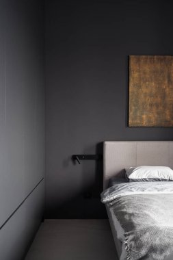 Element of comfortable bed in hotel bedroom. Dark grey wall with reading light lamp and art painting over sleeping space. Apartment with loft style design clipart