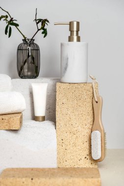 Güzellik ürünlerini doldurulabilir sabun şişesi ile tanıtmak için podyum, el kremi ile tüp, primus taşı, pamuk yüz havlusu ve banyoda bitki dalı olan cam vazo.