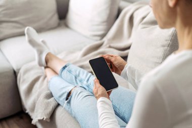 Akıllı telefonda boş ekranlı internet uygulaması kullanan bir kadın. Arka ve omuz üstünden kadın hızlı ve güvenilir internet bağlantısını kullanıyor cep telefonuyla evde boş zaman geçiriyor, kanepede yatıyor.
