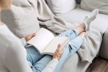 Evde kitap okuyan bir kadının omuz üstü görüntüsü. Tasasız bir kadının arka plandaki rahat koltukta yatışı, kişisel günlüğünün sayfalarını çevirmesi. İlham, hayal gücü ve eğlence kavramları