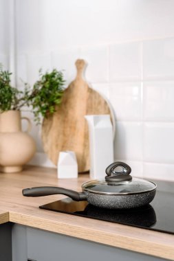 Mutfaktaki modern elektrikli sobanın kapağıyla seçici bir şekilde kızartma tavasına odaklan. Cam seramik fırının tepesinde yemek hazırlıyorum. Yemek pişirme konsepti. Mutfak eşyalı ev aletleri.