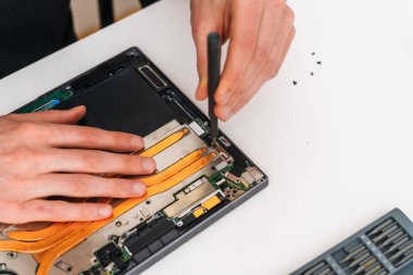 Adam tornavidayla elektronik cihazı tamir ediyor. Laptop servisinde çalışan bir tamirci. İşçi kırık parçaları bilgisayardan kaldırır, ana kartı netbook 'a yükseltir, dijital tabletteki pili değiştirir