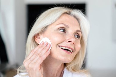 Cilt bakımı için yaşlanma karşıtı tedavi. Güzelliğin bakıma ihtiyacı var. Kadın portresi günlük ameliyatlar yapıyor, yüz derisini doğal losyonla temizliyor, pamuk disk sünger pedi kullanıyor, makyaj malzemelerini çıkarıyor.